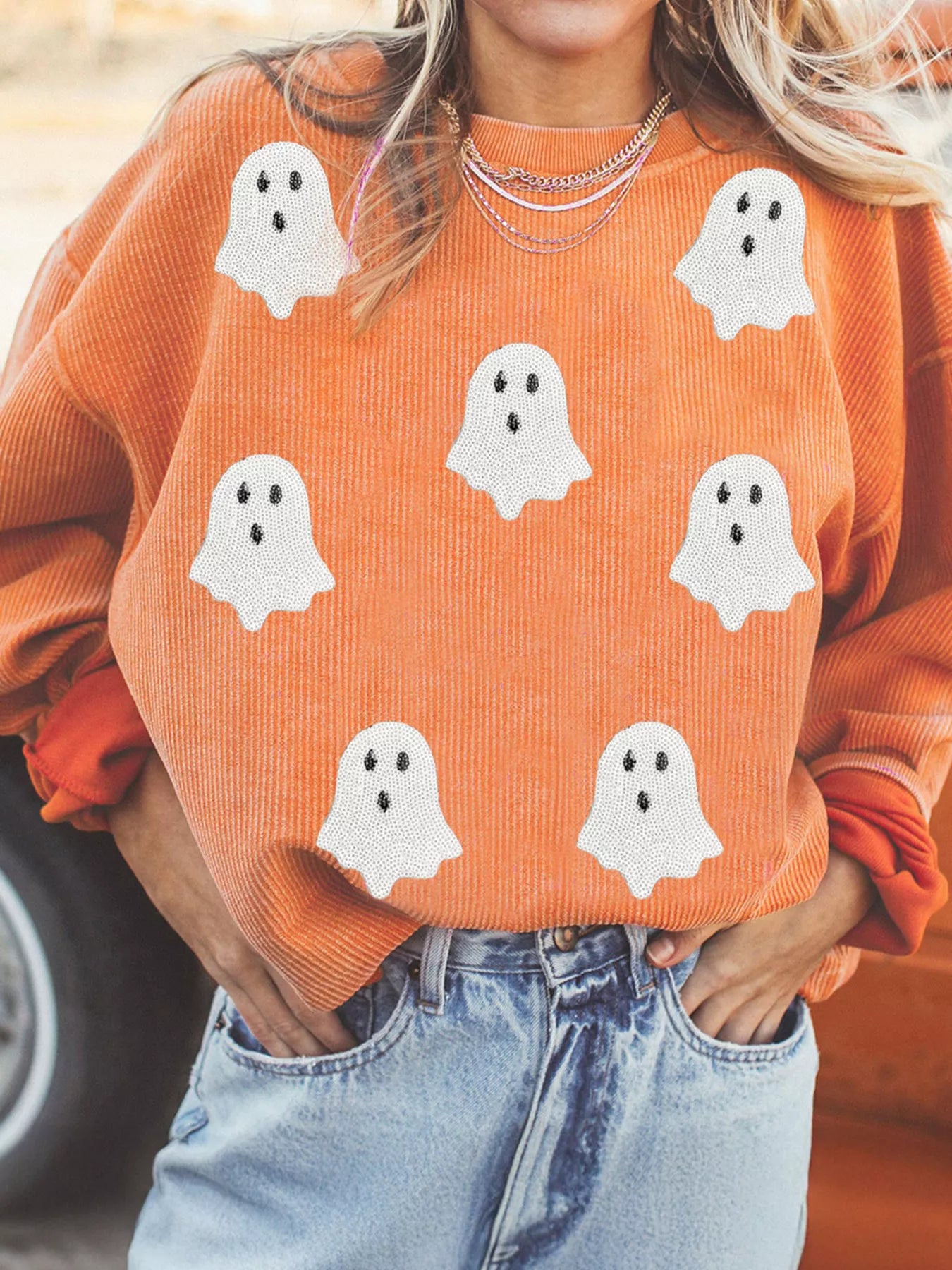 Orange corduroy sweater with white ghost prints, paired with denim jeans for Halloween fashion